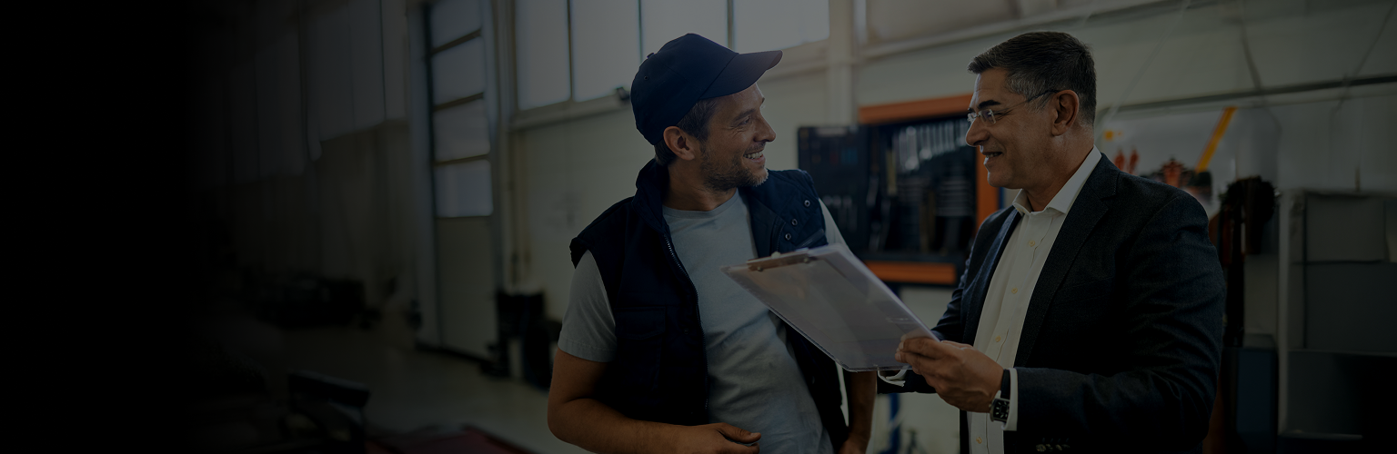 Two workers talking over a clipboard in a service garage.