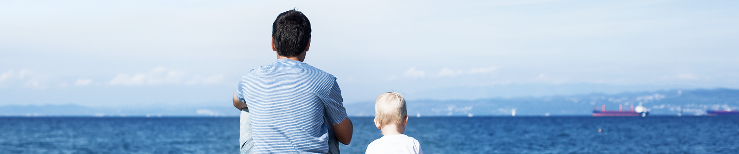 Father and toddler sitting by a lake and looking out at the view.