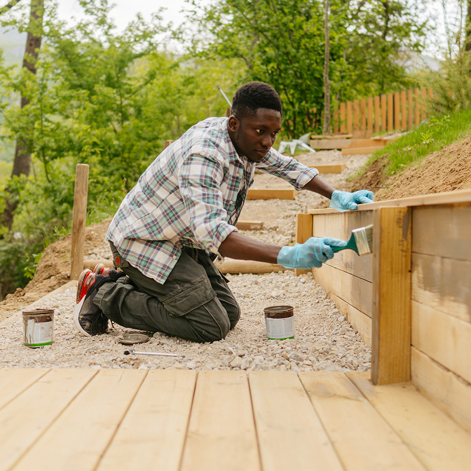 A man painting a wooden retaining wall