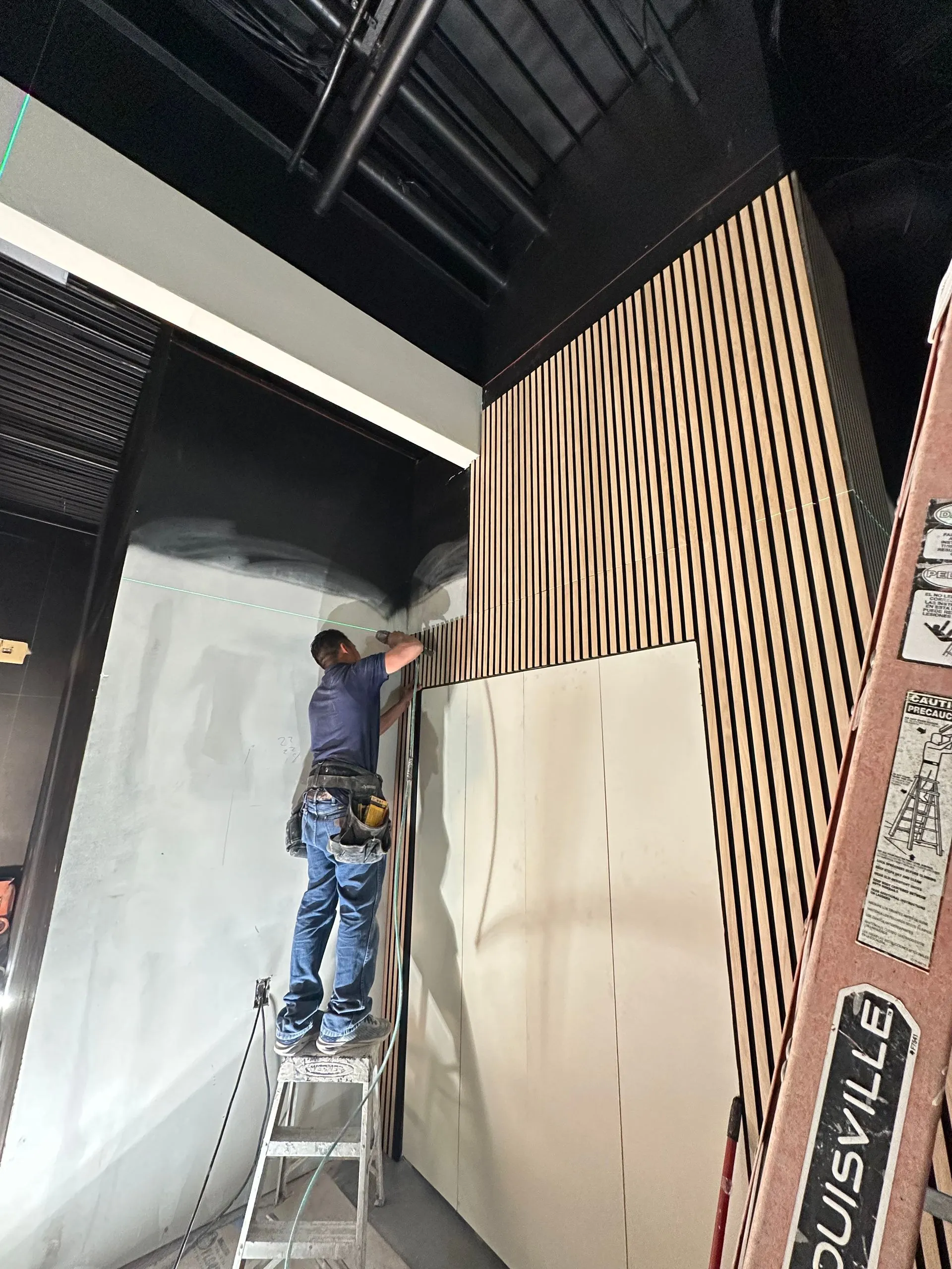 Craftsman installs decorative wood slat wall panels inside a modern commercial space, enhancing arch 