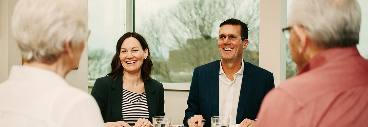 Sue Senio and Brad Weatherill talking with clients at a boardroom table.
