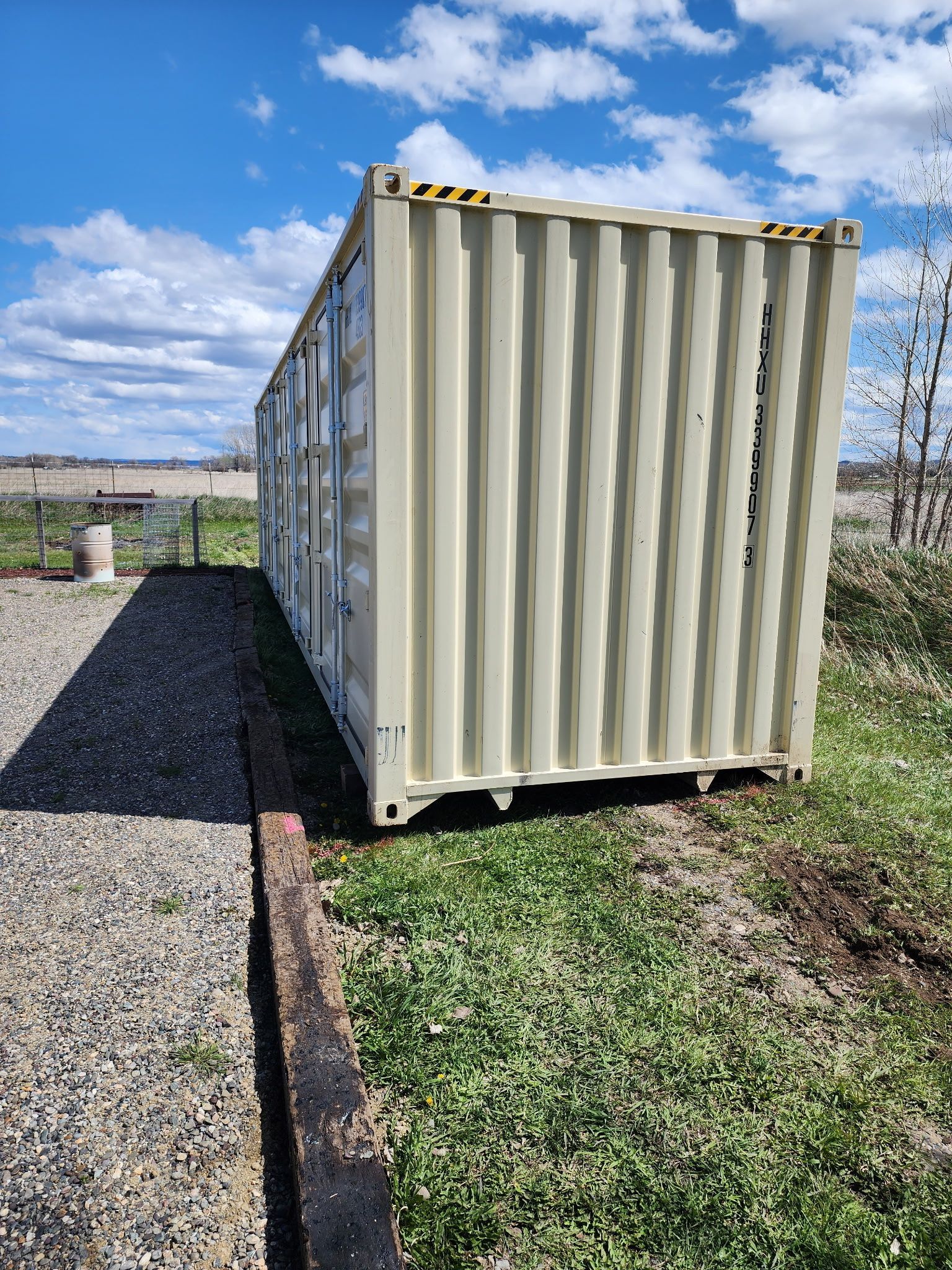 Portable storage container placed outdoors on grassy area beside gravel driveway, featuring durable steel construction and secure locking doors, ideal for onsite storage, equipment protection, and residential or commercial use.