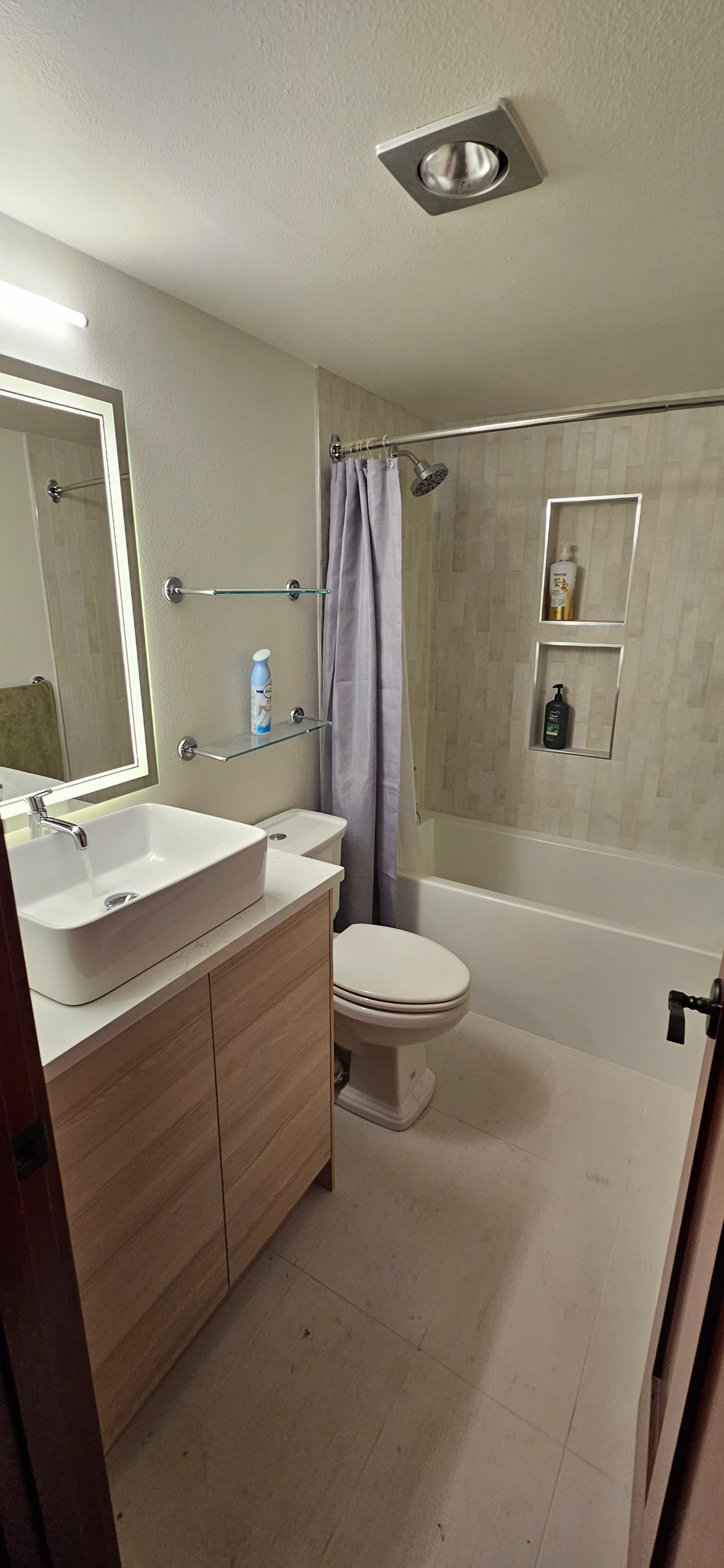 Modern bathroom featuring a vanity with vessel sink, wall mirror with lighting, toilet, and bathtub  