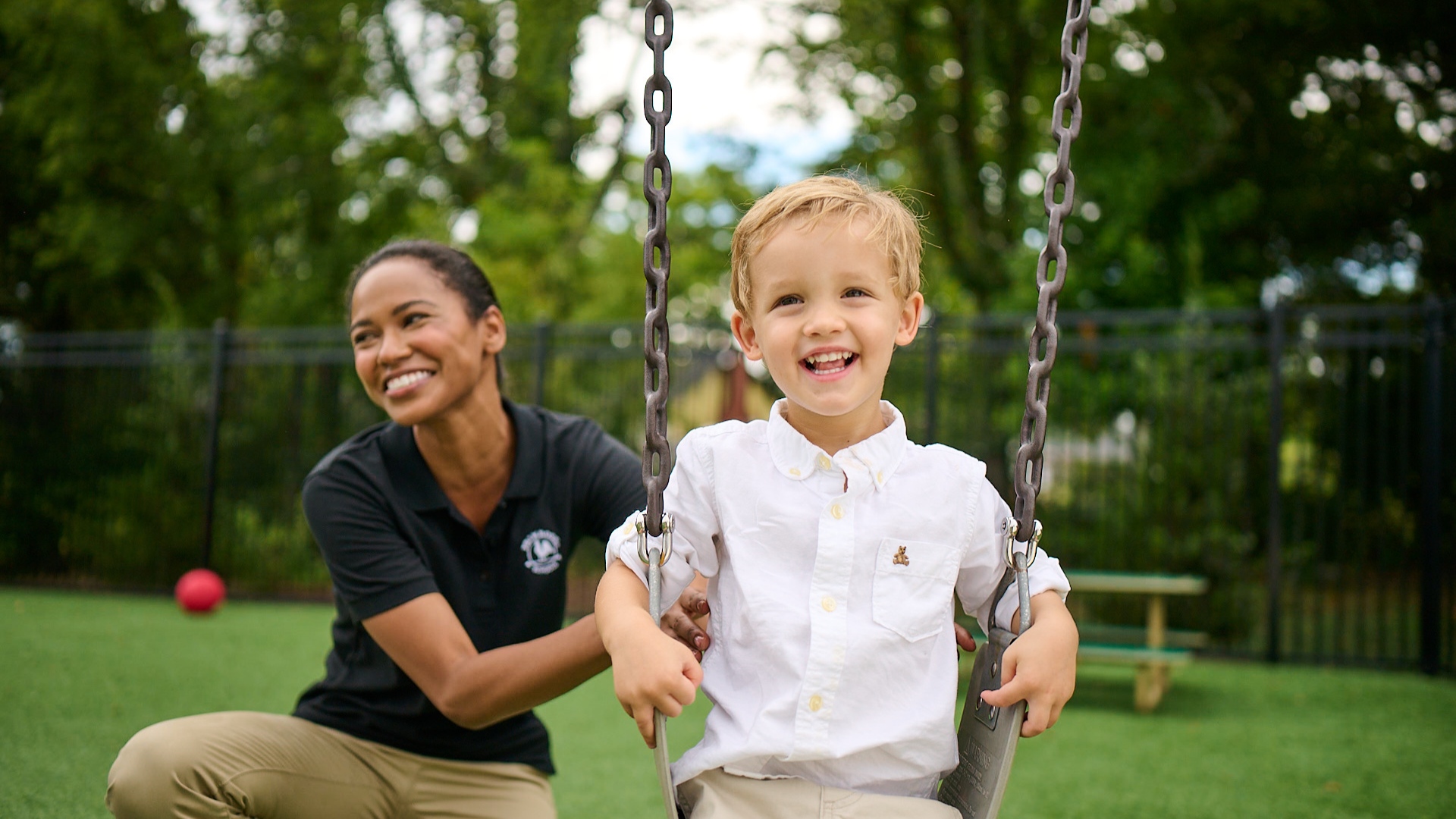 Primrose Schools teacher pushing laughing boy on swing at outdoor childcare playground