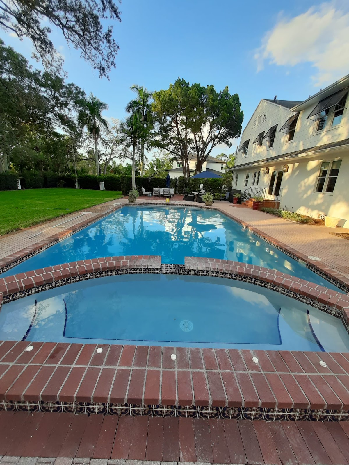 Large residential swimming pool with an attached spa, brick coping, landscaped lawn, and a spacious backyard setting.