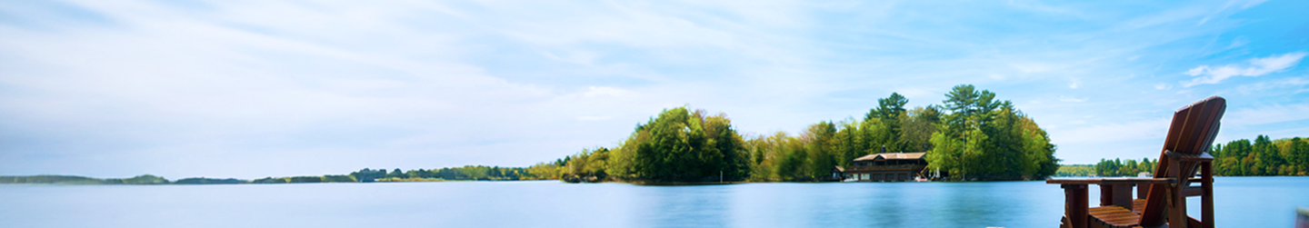 A red Muskoka chair on a dock overlooking a calm lake.