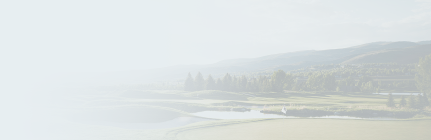 A golf course in the afternoon sun, with mountains and trees lining the perimeter.