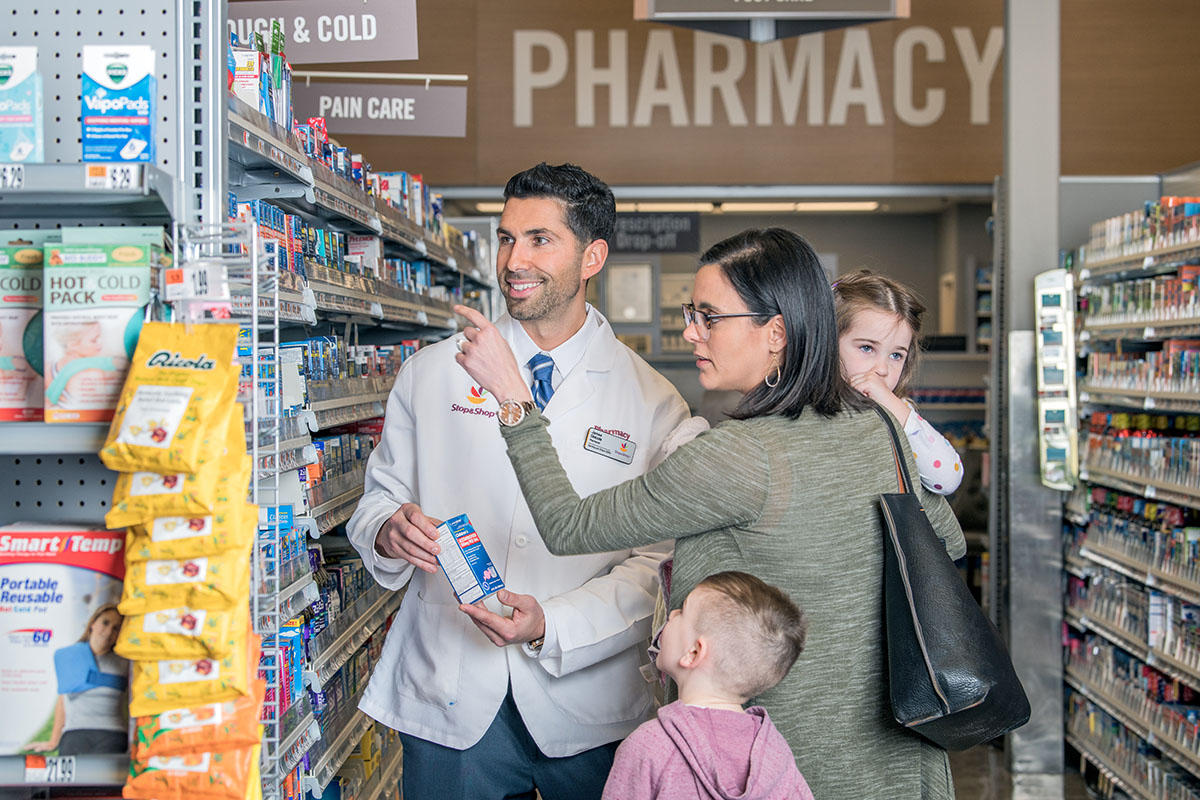 Customer with children asking advice from pharmacist in aisle.