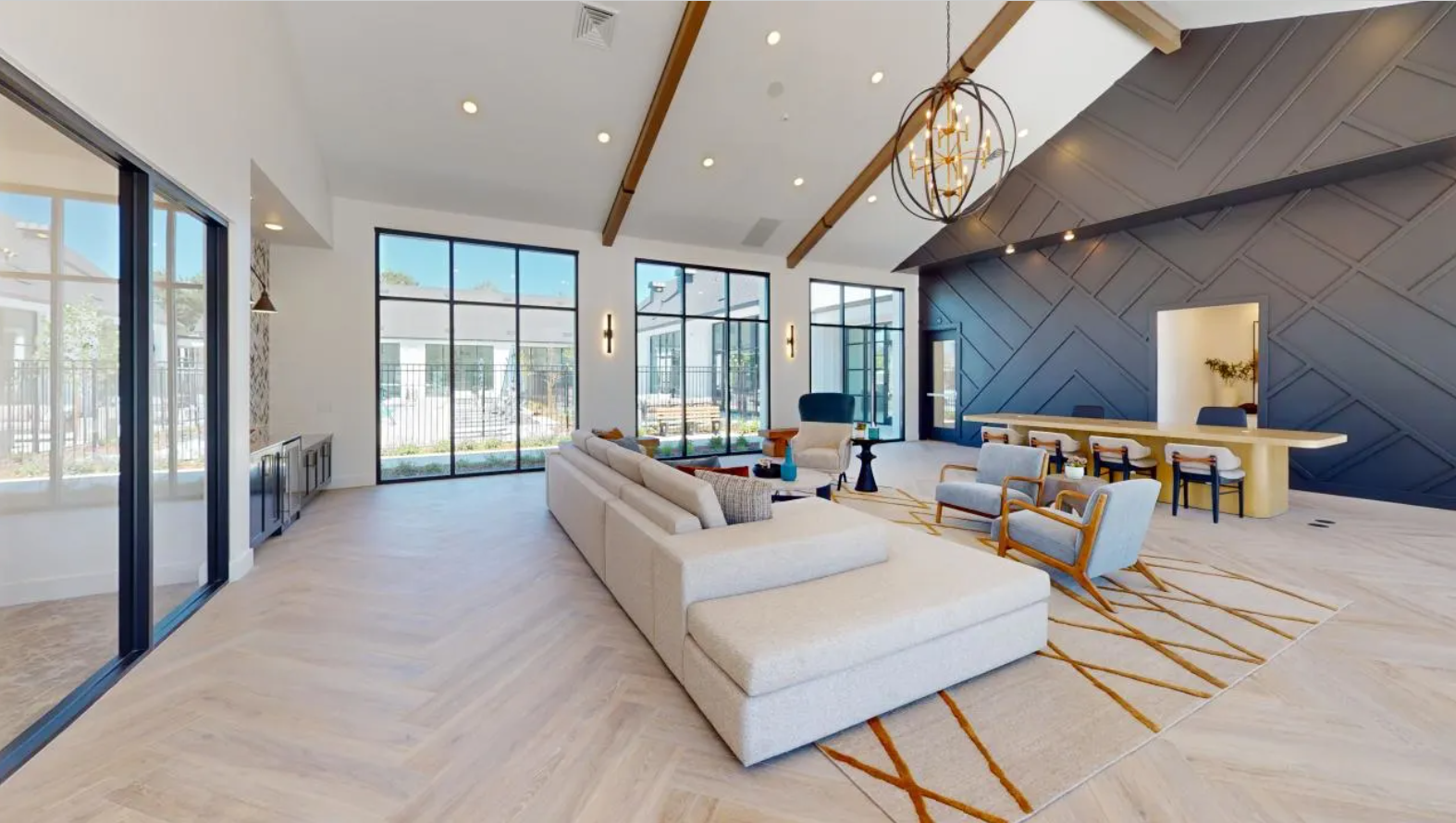 Resident lounge area with herringbone wooden flooring, a cream couch, and a large table surrounded by chairs