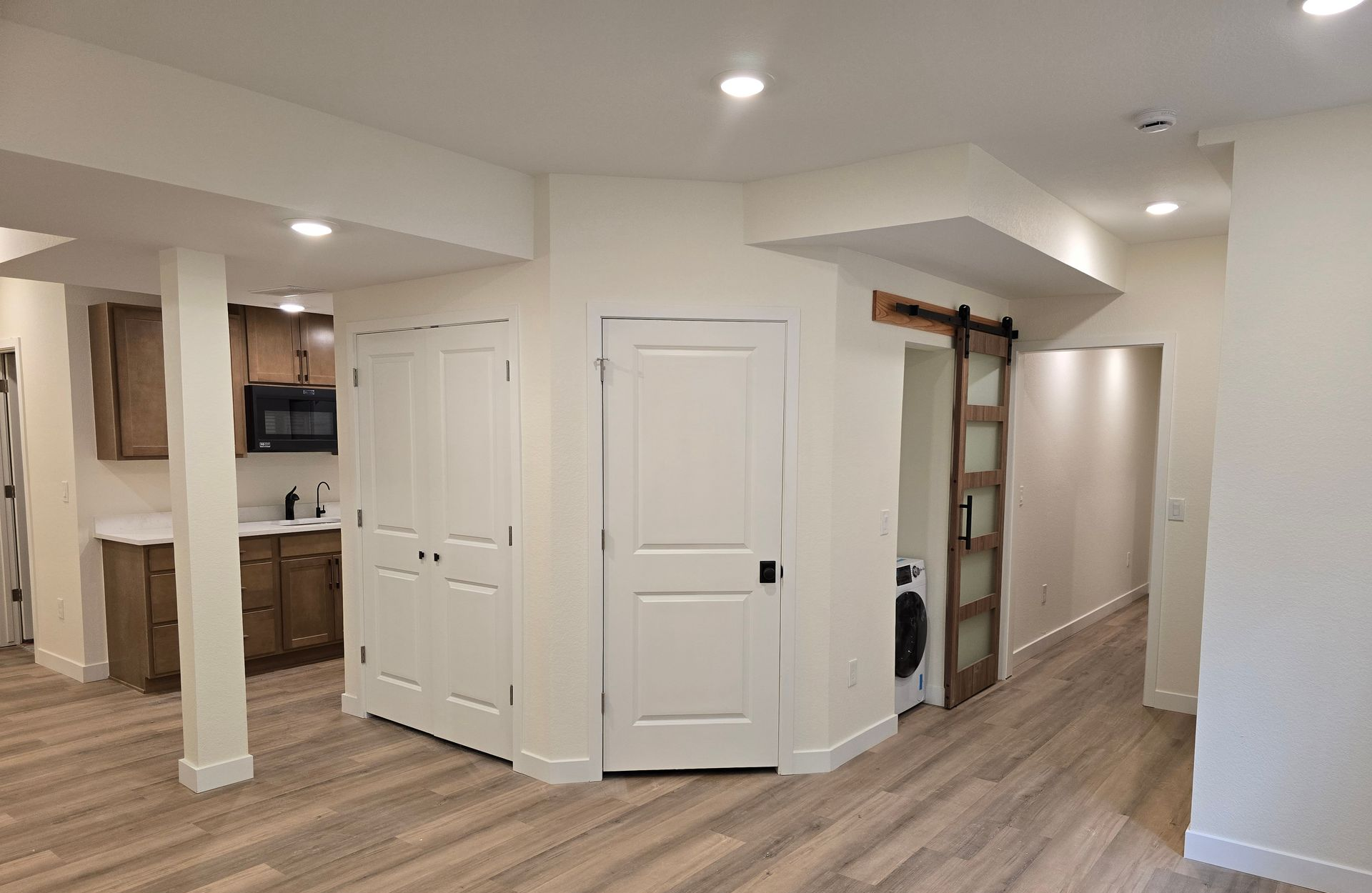 Open-concept finished basement featuring luxury vinyl plank flooring, recessed lighting, storage doors, laundry area, and kitchenette access, showcasing a clean, organized, and highly functional living environment.