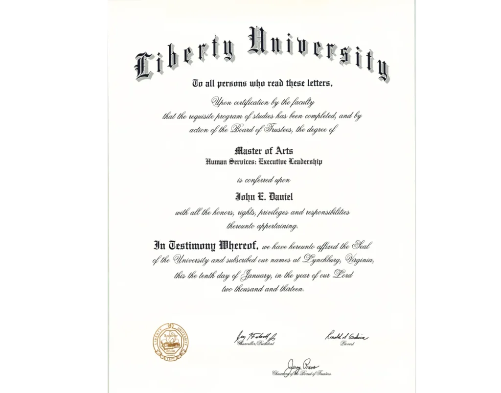 A close-up of a Liberty University diploma for a Master of Arts degree in Human Services: Executive Leadership, conferred upon John E. Daniel on January 10, 2013. The diploma features the university's name in ornate lettering at the top, followed by official text detailing the degree conferral. It includes signatures and seals at the bottom, signifying its authenticity.