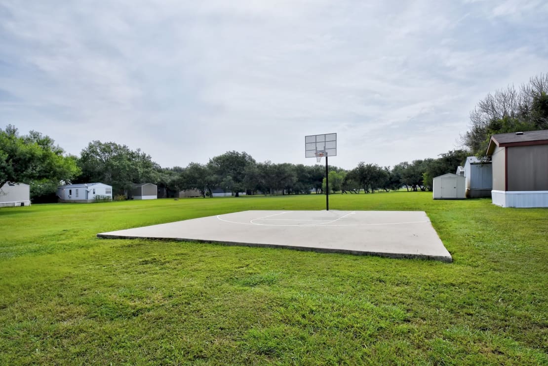a basketball court sits in the middle of a grassy field