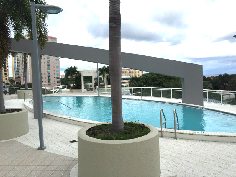 Contemporary commercial or condominium swimming pool with palm trees, white decking, and surrounding residential buildings.