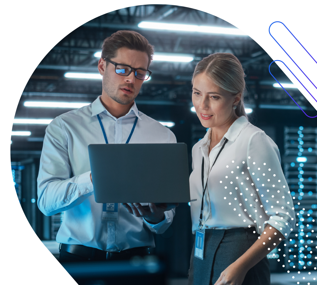 A man and a woman in a server room looking at a laptop. The man is wearing glasses and a light blue collared shirt with a lanyard. The woman is wearing a white collared shirt and a gray skirt with a lanyard. The server room is dimly lit with rows of server racks visible in the background. There are abstract blue and purple lines in the upper right corner and white dots scattered across the right side of the image.