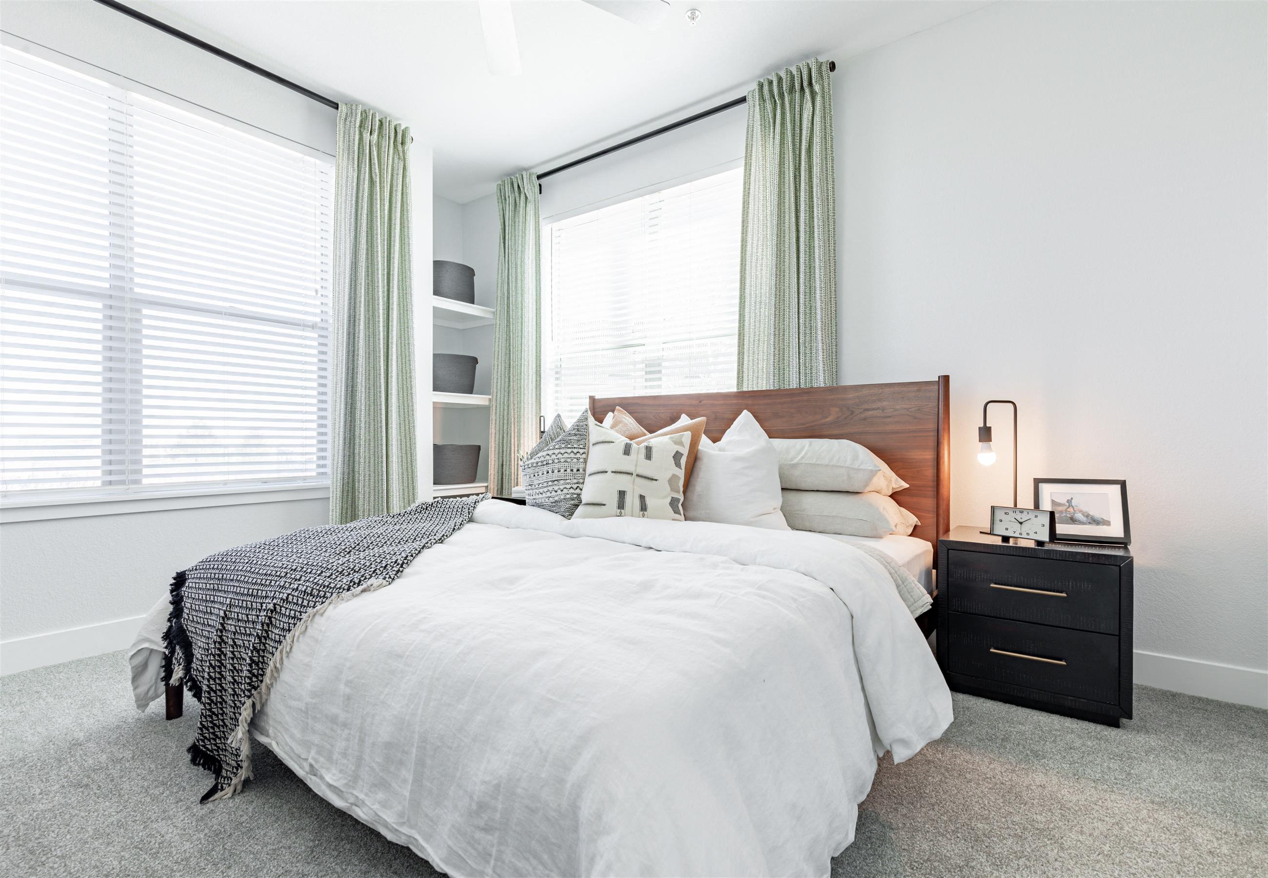 a bedroom with two windows and a bed with a white comforter and pillows