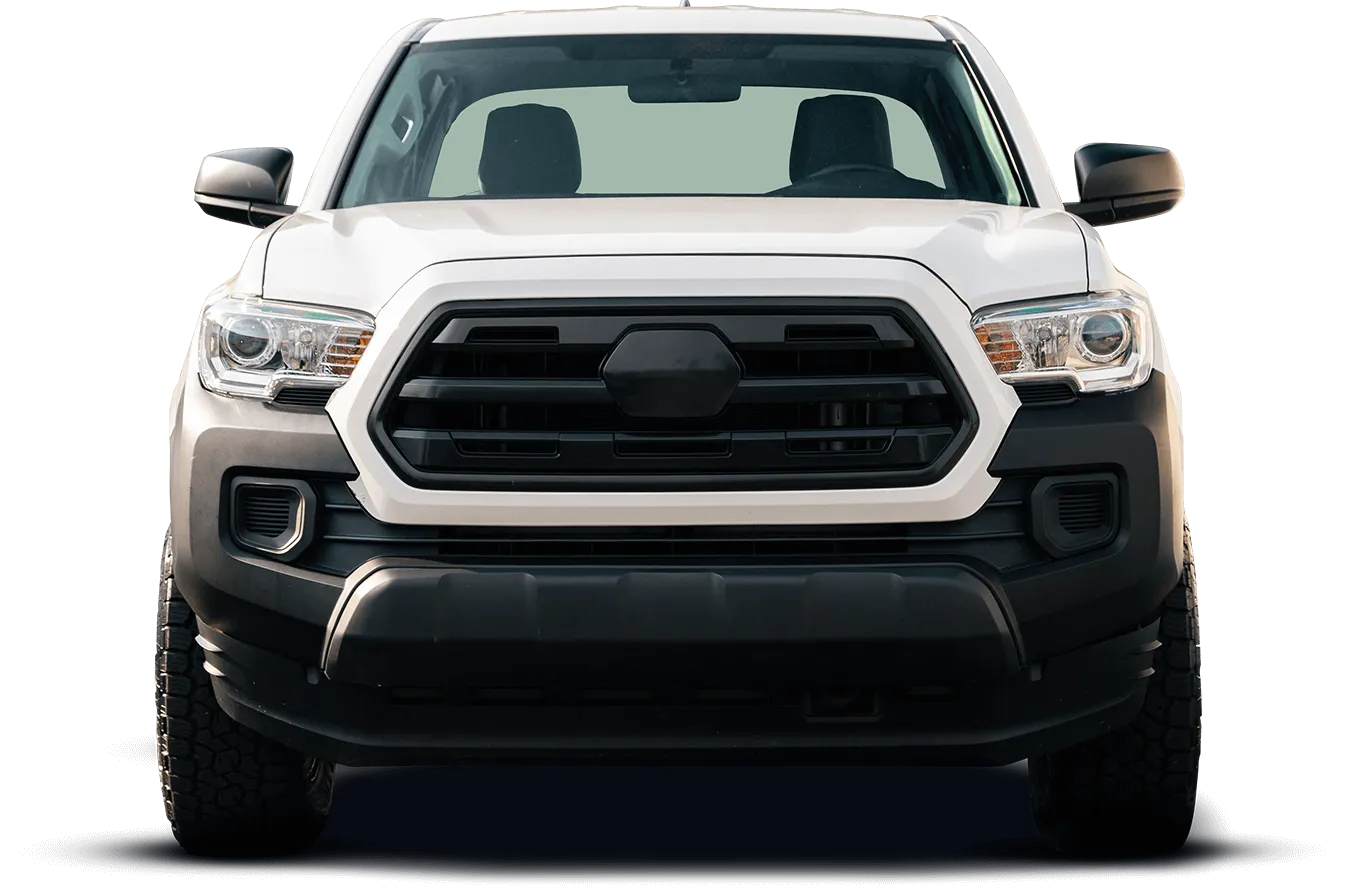 Front view of a white Toyota Tacoma truck with a black grille and bumper, set against a dark background. The headlights are illuminated.