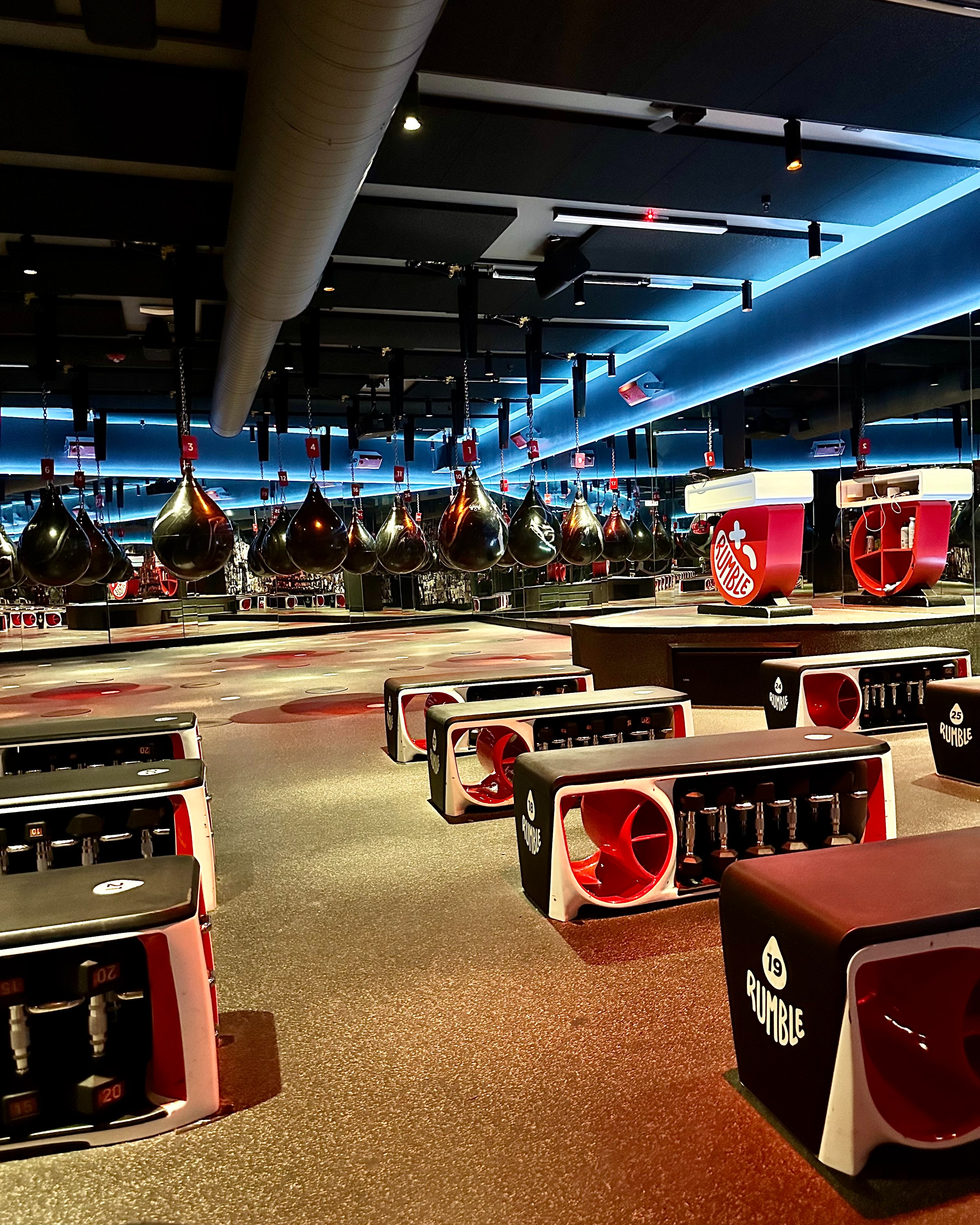 Rumble studio with strength training benches and dumbbells in the foreground and the boxing side aqua bags in the background.