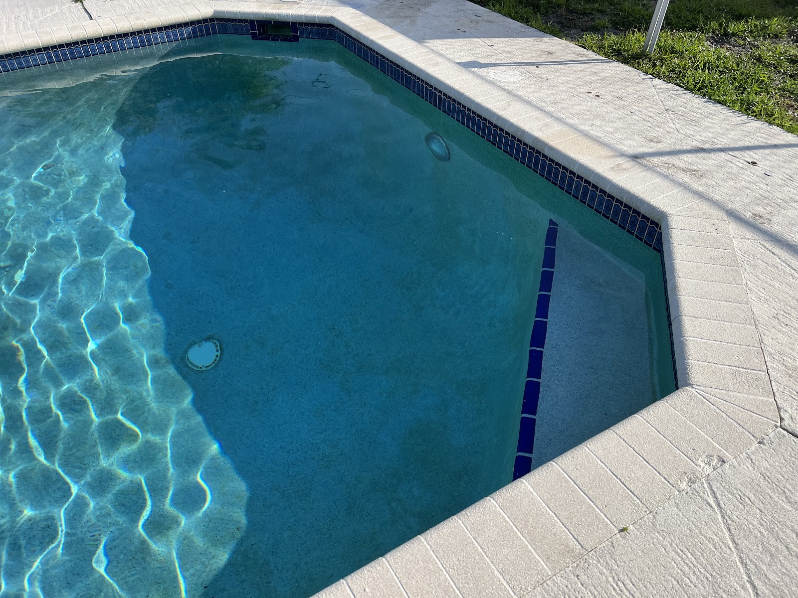 Close-up of a residential swimming pool corner with sparkling blue water, decorative tile, and light stone coping.