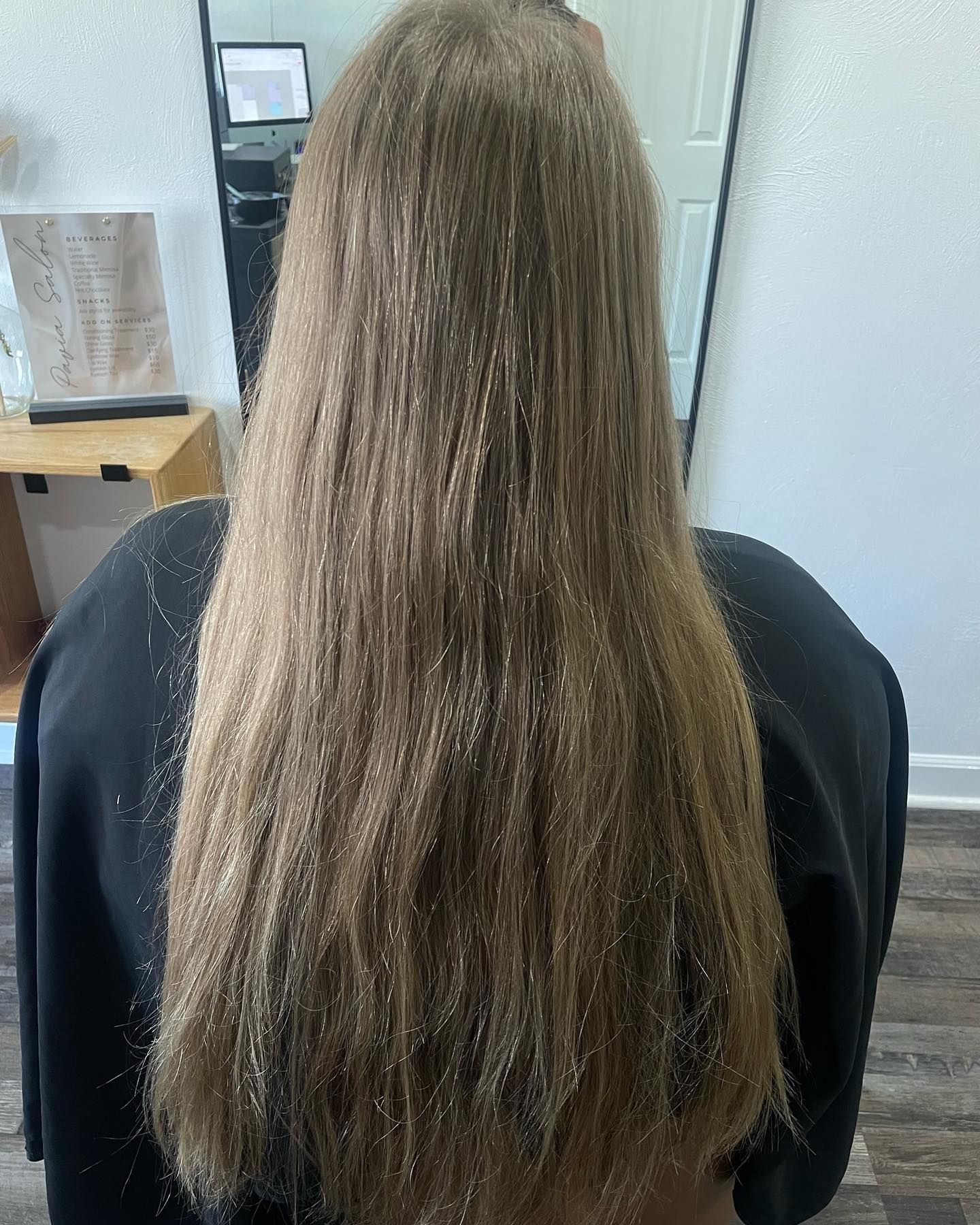 Back view of long straight light brown hair before styling, showing natural texture and length in a professional salon setting.
