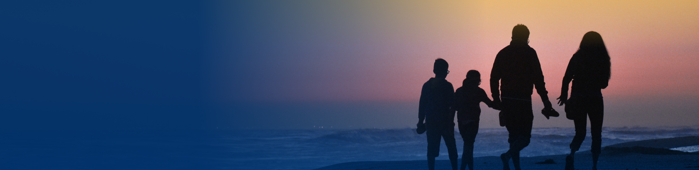 Silhouettes of a family of four walking side by side along the beach shore at sunset.