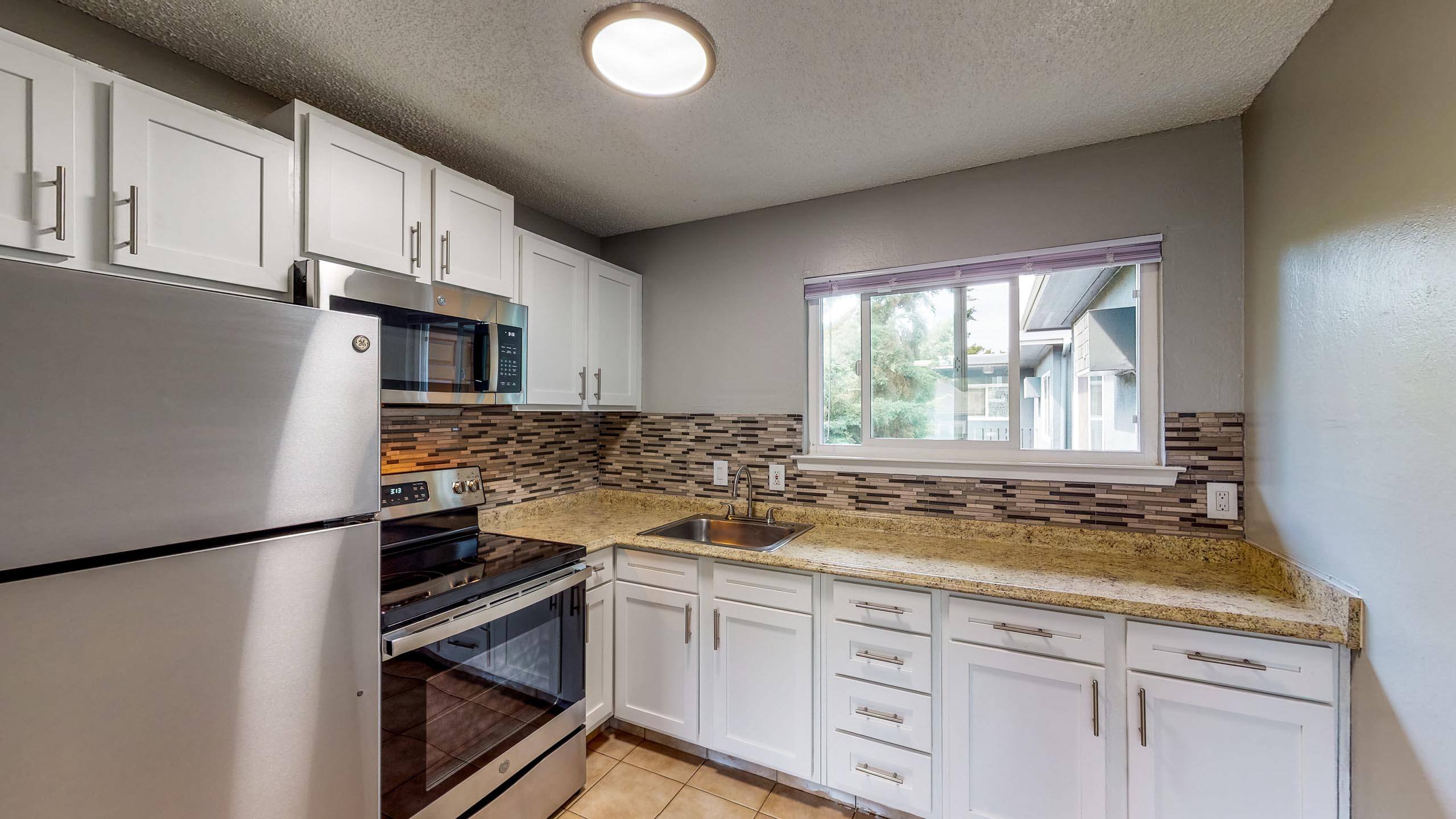 A kitchen with white cabinets and a granite countertop at University Square Apartments, California 95616