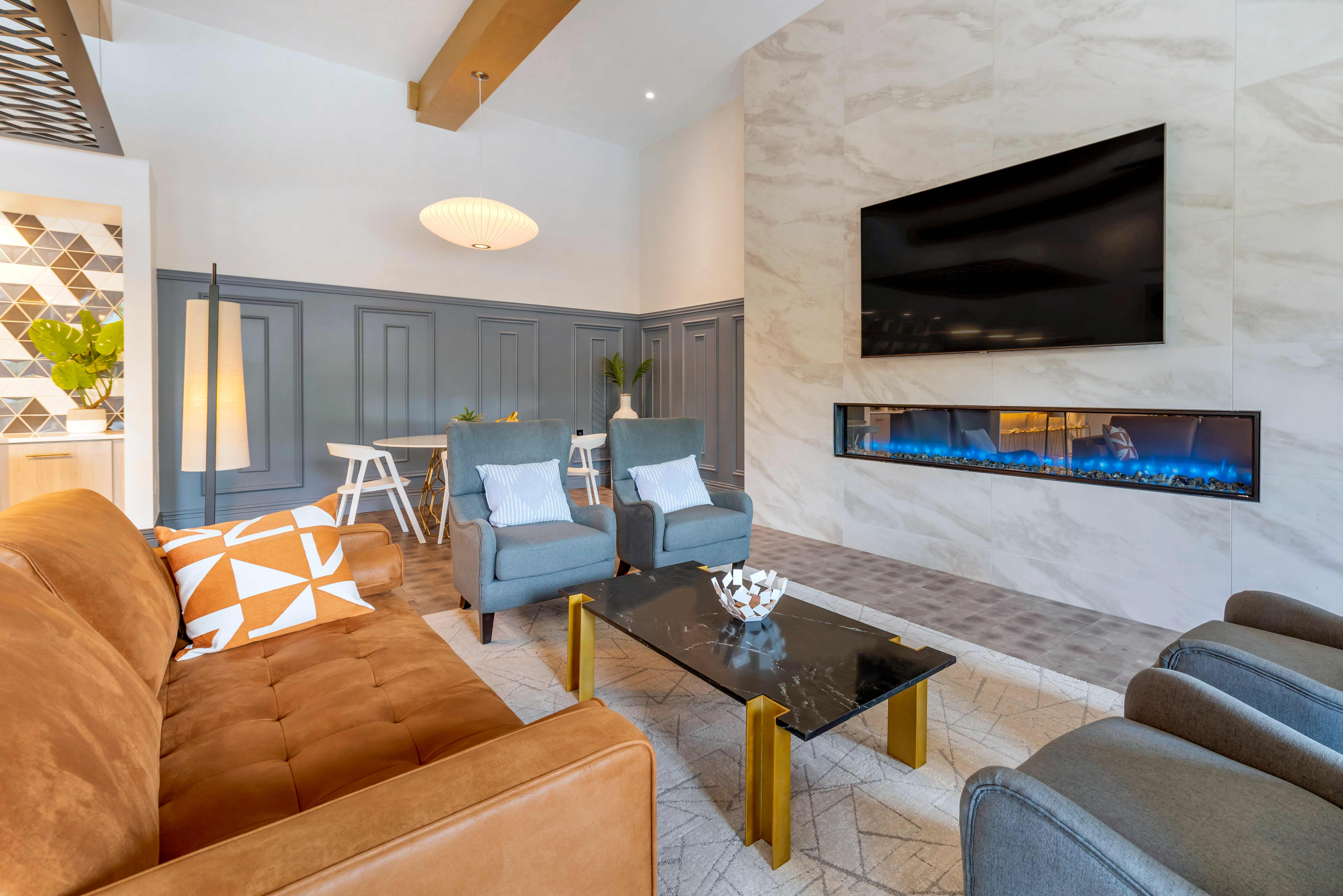 Resident clubhouse with television, couch, armchairs, and modern fire feature.