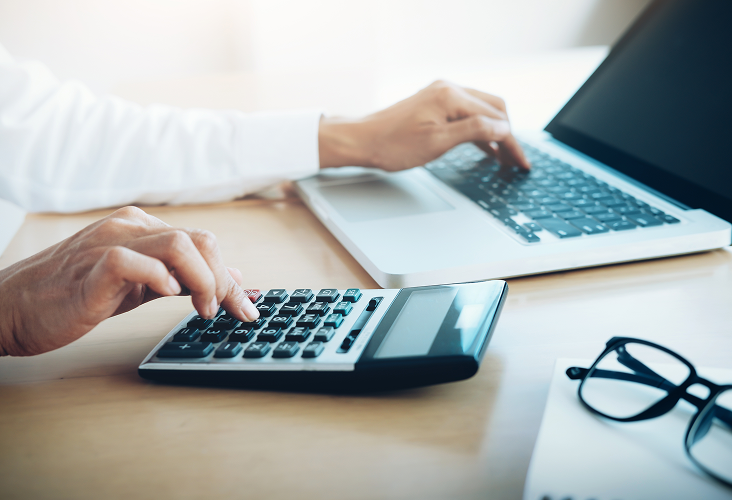 An individual typing on a laptop and calculator.
