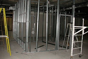 An interior view of a building under construction with exposed steel framing and scaffolding. The unfinished space shows the framework for walls and ceilings, representing the early stages of a structural build or restoration project.