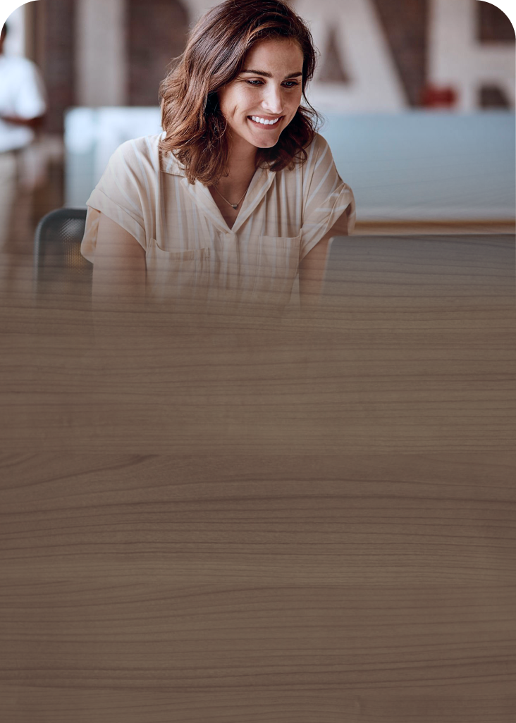 A woman smiling as she looks at her laptop screen.