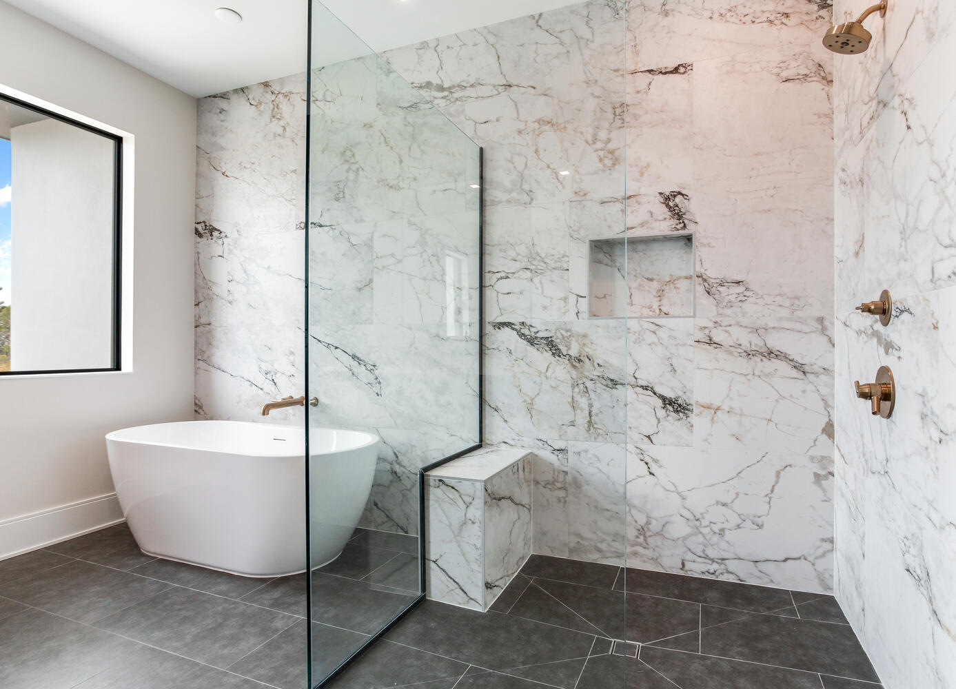 Elegant spa-style bathroom with a freestanding soaking tub, walk-in shower, marble-look tile, built-in shower niche, and premium modern fixtures.