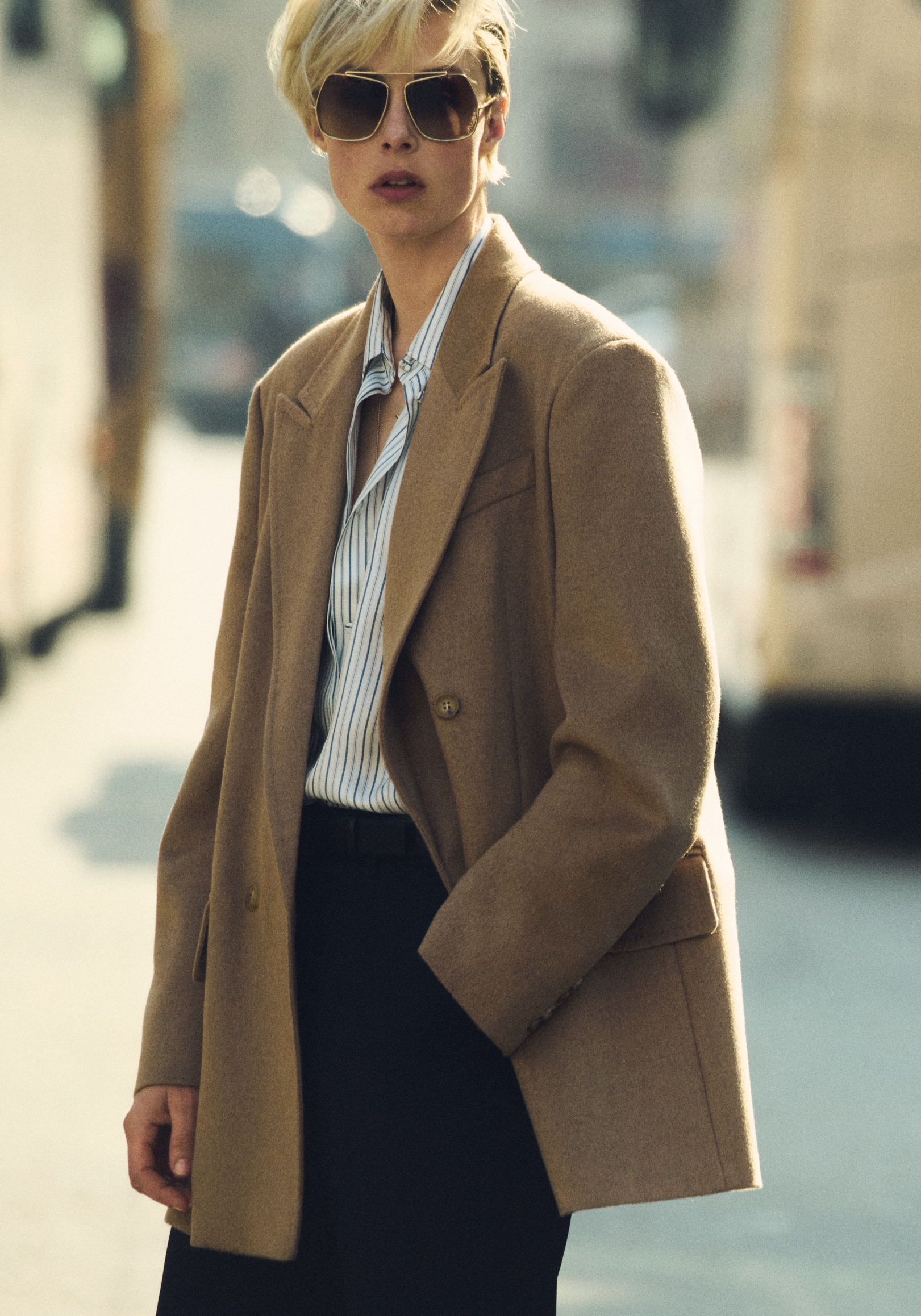 Mannequin portant le blazer double boutonnage Olimpia Jacket de Max Mara couleur chameau avec des lunettes de soleil et une chemise en milieu citadin.
