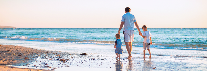 A father walking hand in hand with his two children along the beach.