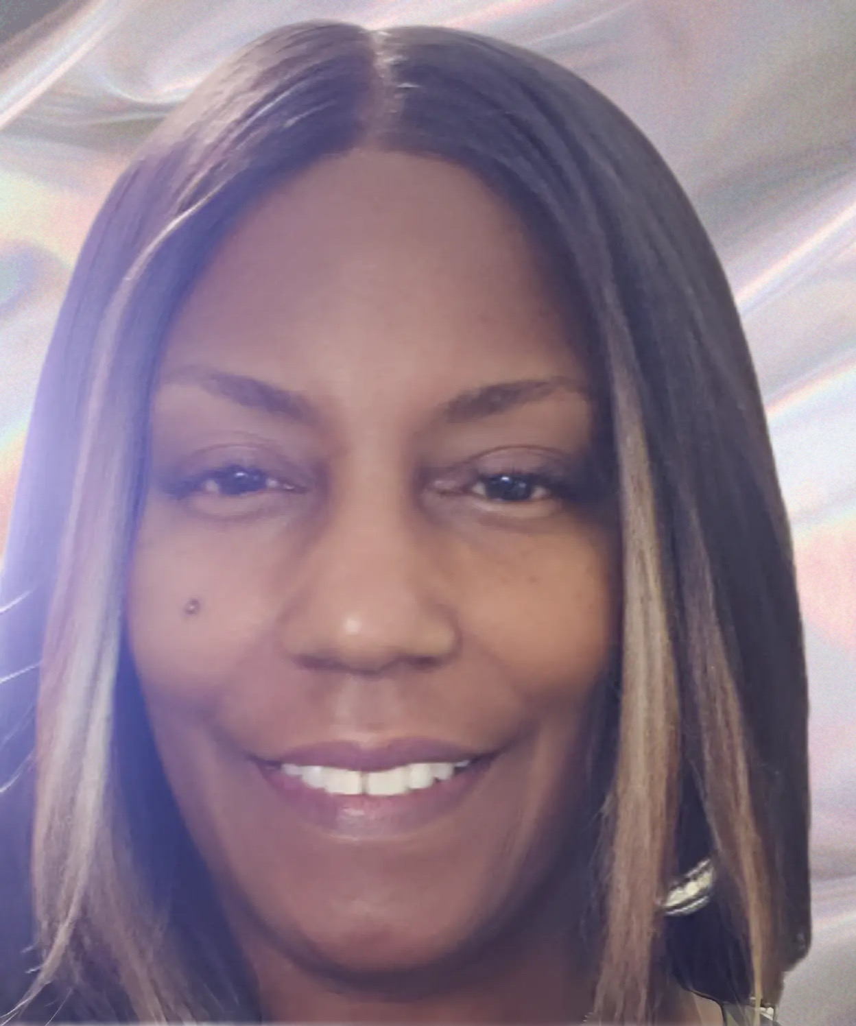 A close-up portrait of a Black woman with long, dark hair with blonde highlights. She has brown eyes 