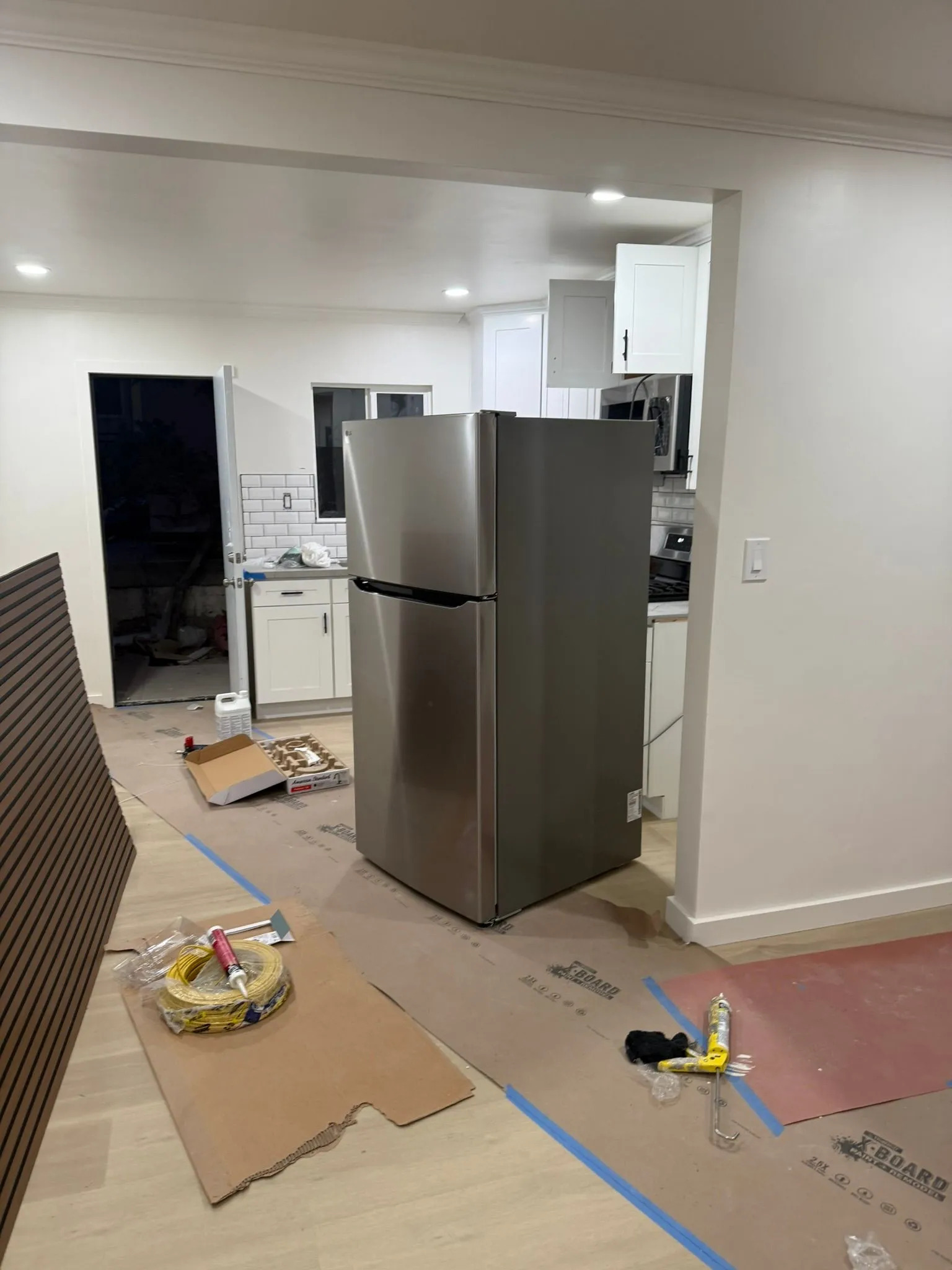 Residential kitchen remodeling project nearing completion with white cabinetry, stainless steel refr 