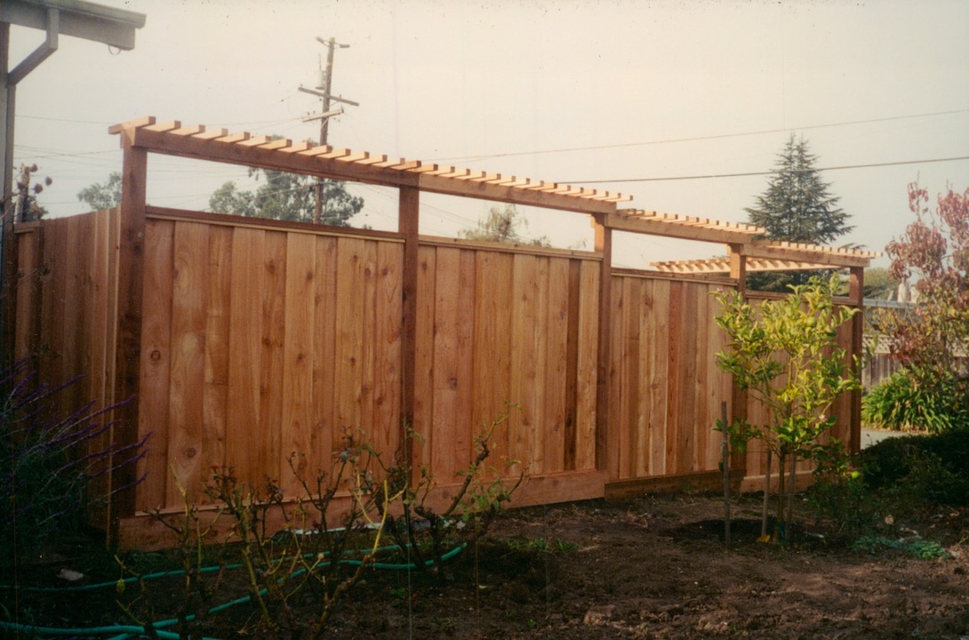 Wood privacy fence with overhead lattice framing, adding structure and privacy to a residential yard.