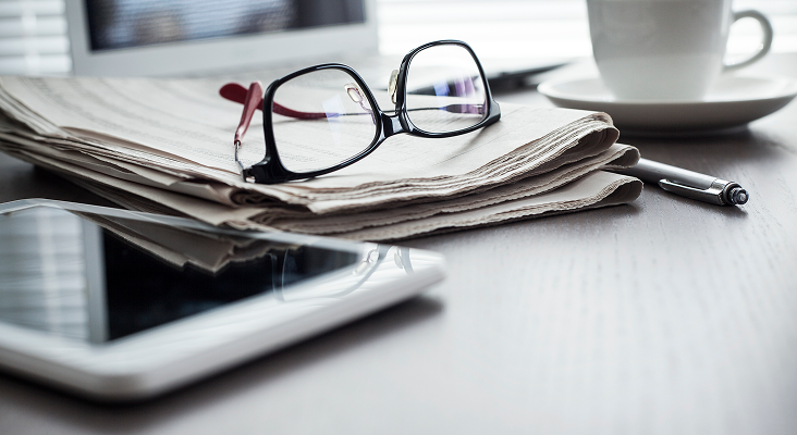 A close up of a folded newspaper with a pair of glasses on top.