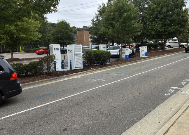 Several EVgo fast charging units installed in marked parking spaces at a public charging station, with EVgo logos on the chargers, protective bollards around each unit.
