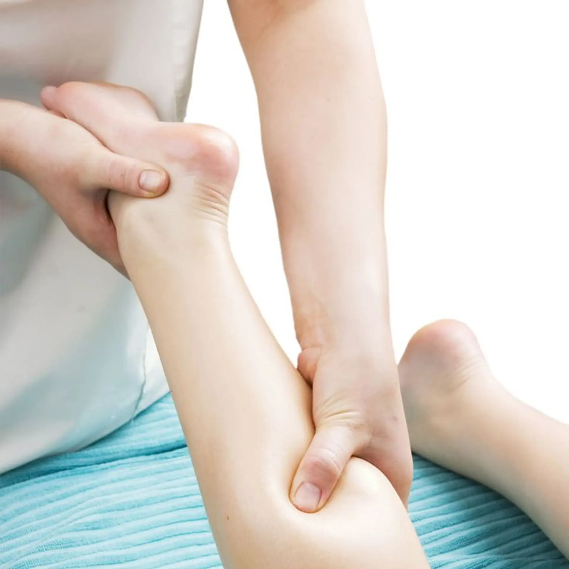A close-up shot shows a person's hands massaging the lower leg and foot of another person. The masseuse's hands are gently gripping and manipulating the calf muscle and the arch of the foot. The recipient's skin is pale, and the scene is set against a white background with a blurred turquoise towel visible at the bottom.