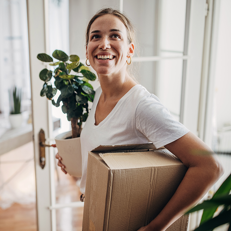 A woman holding a plant and cardboard box.