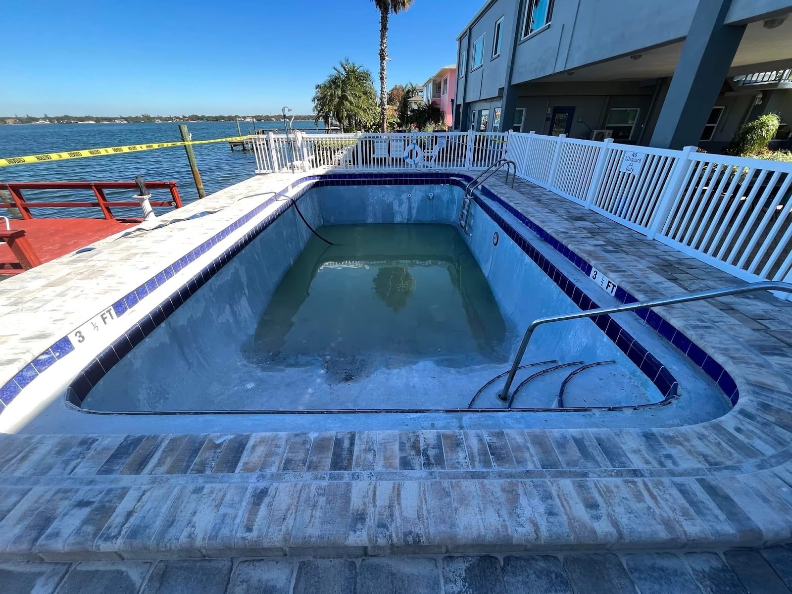 Waterfront swimming pool with light stone decking, white safety railing, and scenic views of the bay.