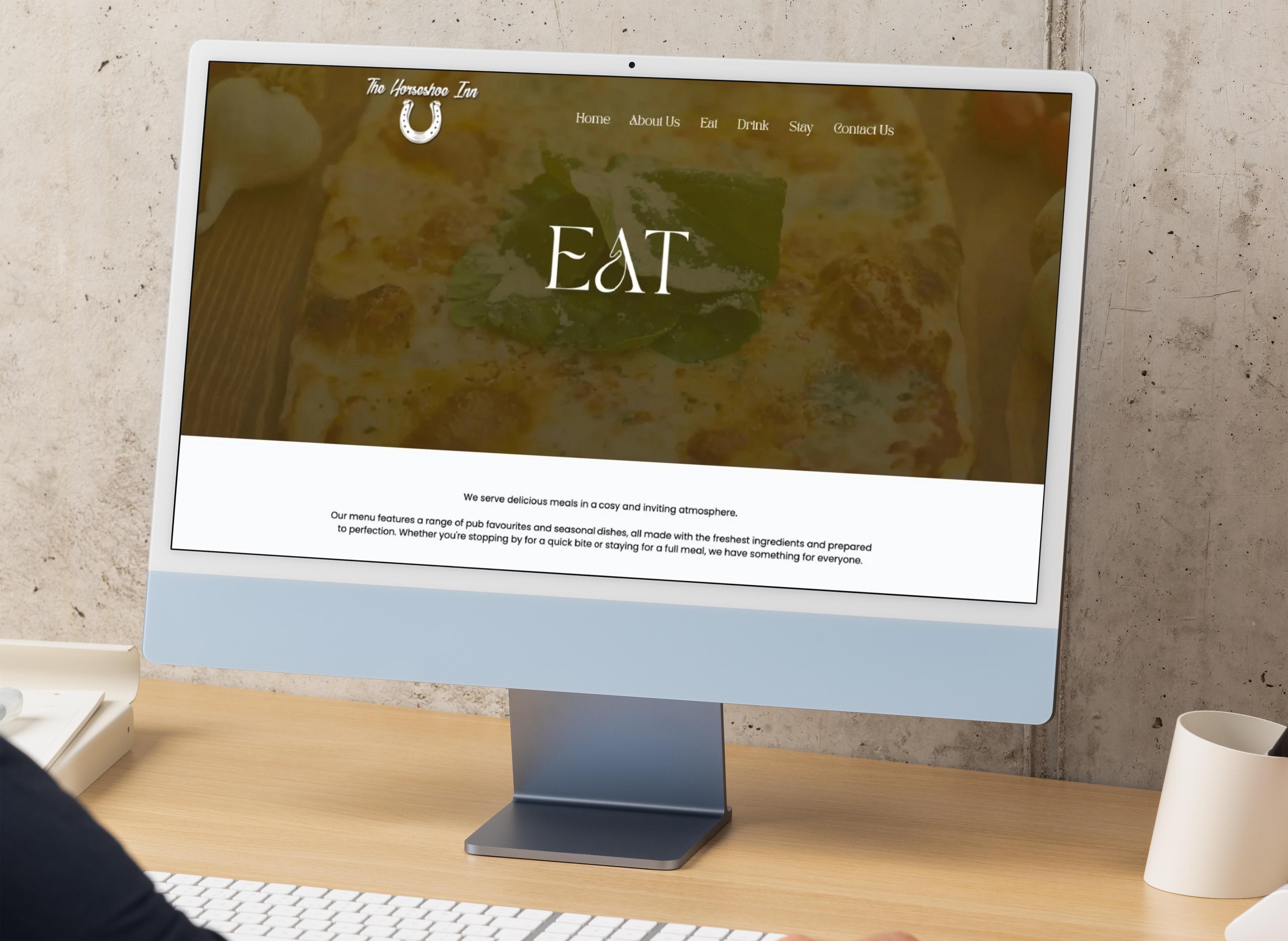 Web design mockup for The Horseshoe Inn pub website displayed on an iMac, showing the Eat page with a food hero image and serif typography.