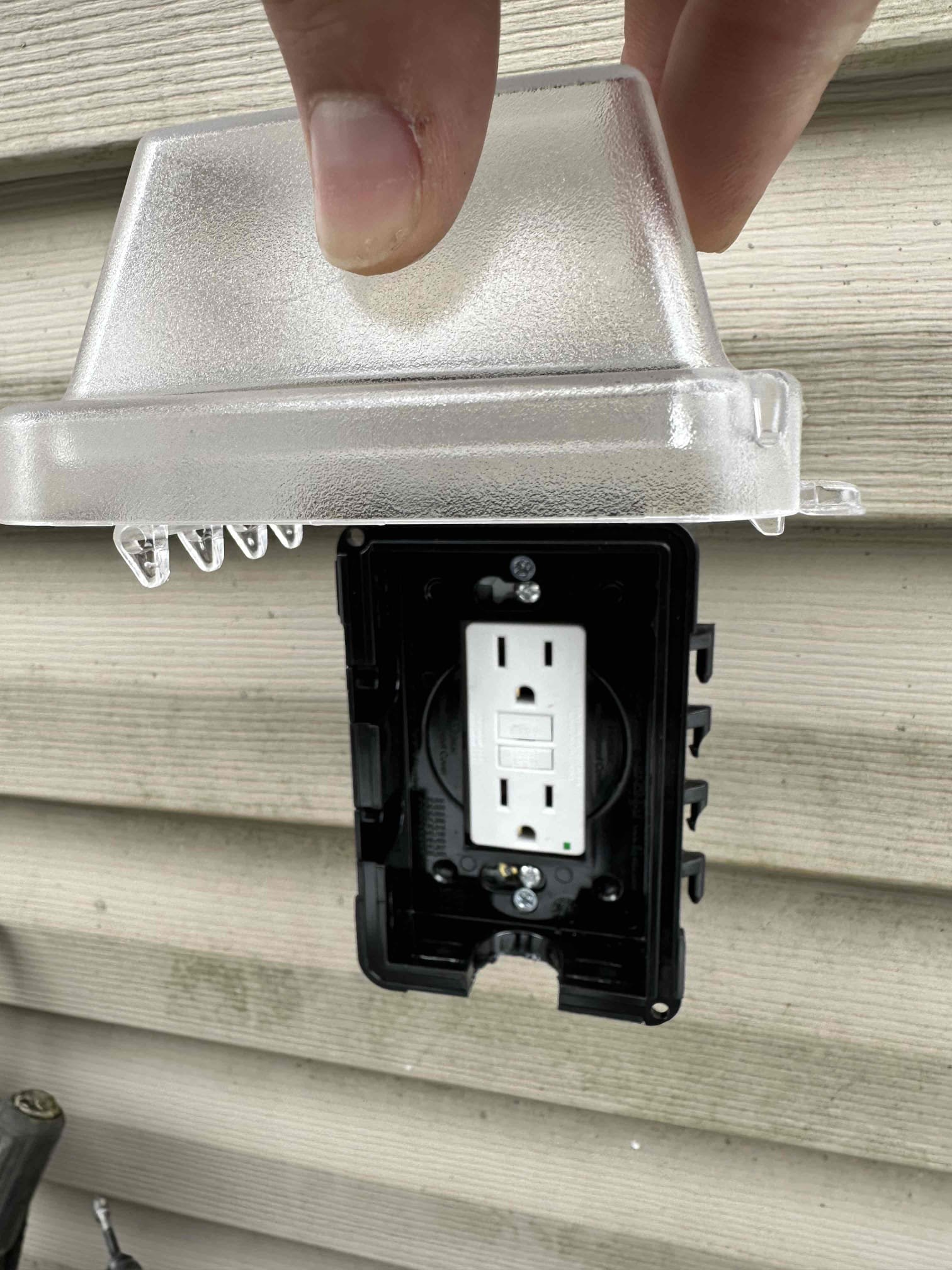 A Thomas Edison Electric technician shows a newly installed outdoor GFCI outlet with a weatherproof in-use cover at a Reading, PA home. The clear bubble cover protects the receptacle from rain and debris while still allowing a cord to stay plugged in.