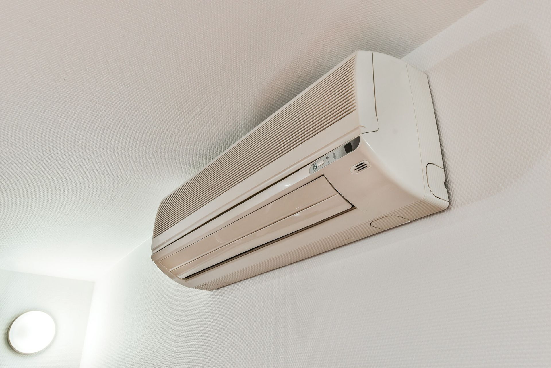 Wall-mounted air conditioning unit installed near ceiling in modern room, providing efficient cooling, airflow control, and temperature regulation, highlighting residential HVAC system design and clean interior environment.