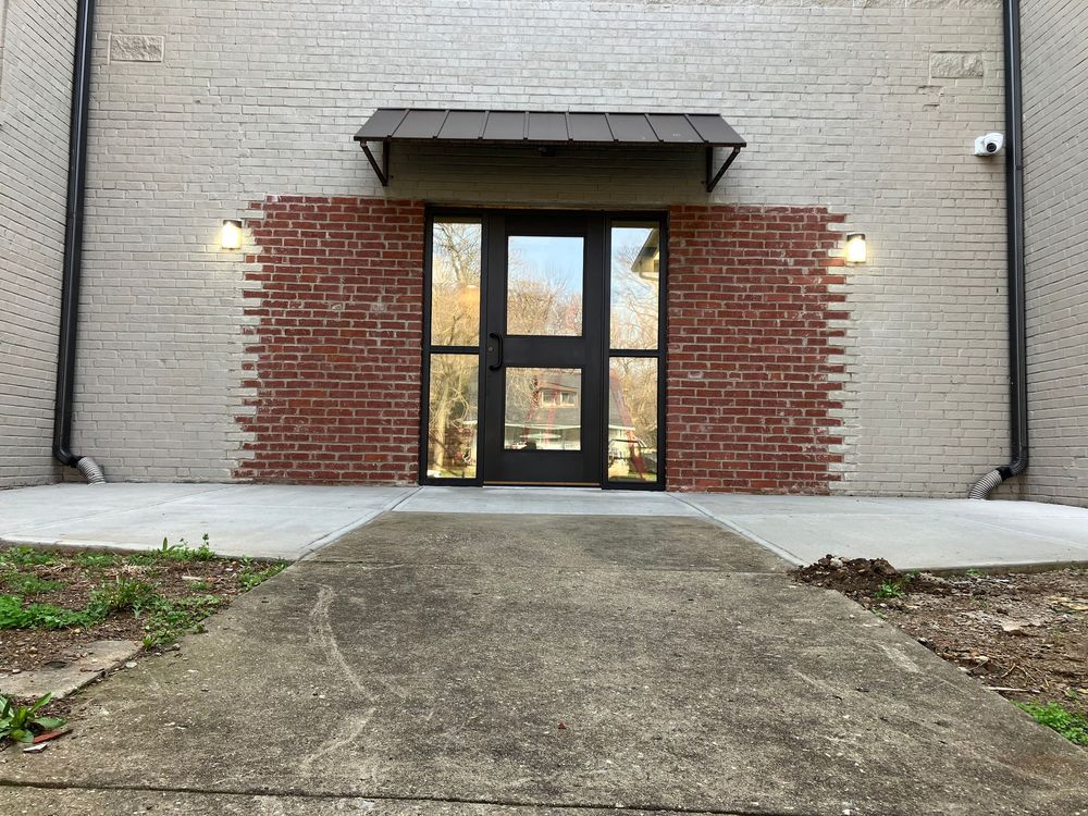 Large commercial building entrance featuring multiple wood doors, glass sidelights, a covered canopy, landscaped planters, concrete walkways, and expansive windows in a contemporary exterior design with durable materials for businesses.