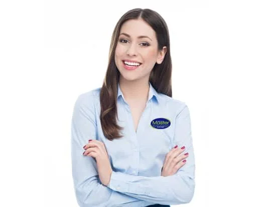 A young woman with long brown hair smiles and stands with her arms crossed, wearing a light blue collared shirt with an oval blue and green logo on the left chest that says "Master" in white letters. She is looking directly at the camera with a friendly expression and has red nail polish on her fingernails. The background is plain white, suggesting a studio setting or cutout image.