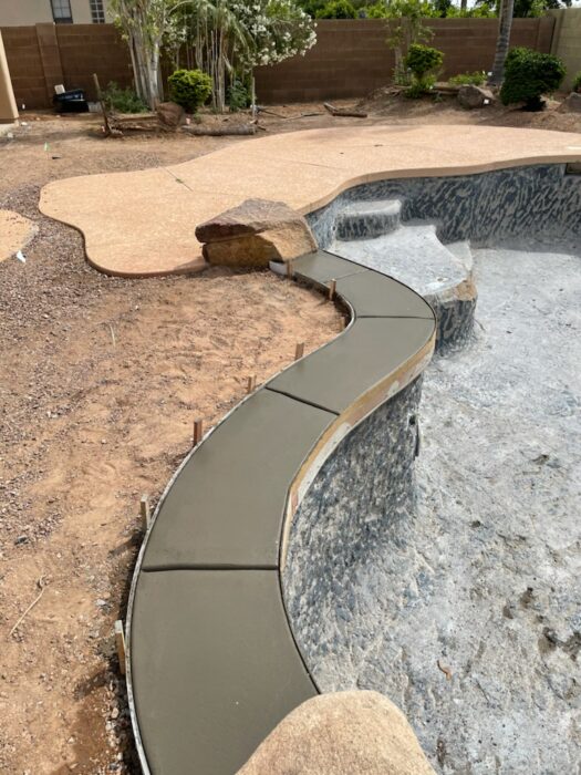 New concrete pool coping being installed along the curved edge of an existing swimming pool during a 