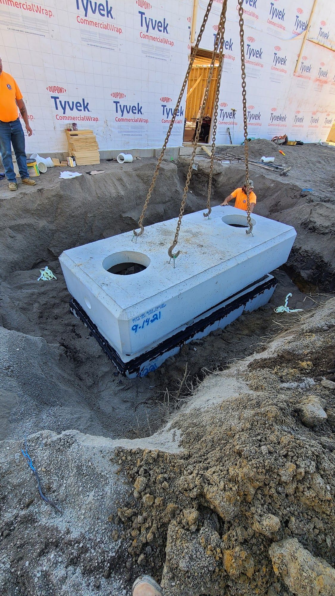 Crew members work inside a protected trench installing underground utility components. Trench shielding and dewatering equipment help maintain safe conditions during excavation activities.