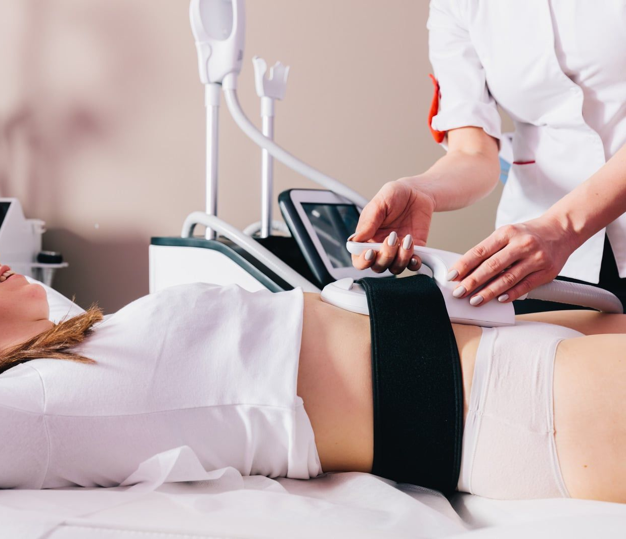 A healthcare professional performs a non-invasive body contouring or weight loss treatment on a patient lying comfortably in a clinical setting. Advanced medical equipment is applied to the abdomen area, highlighting modern wellness technology, cosmetic care, and professional treatment designed for body sculpting and fat reduction.