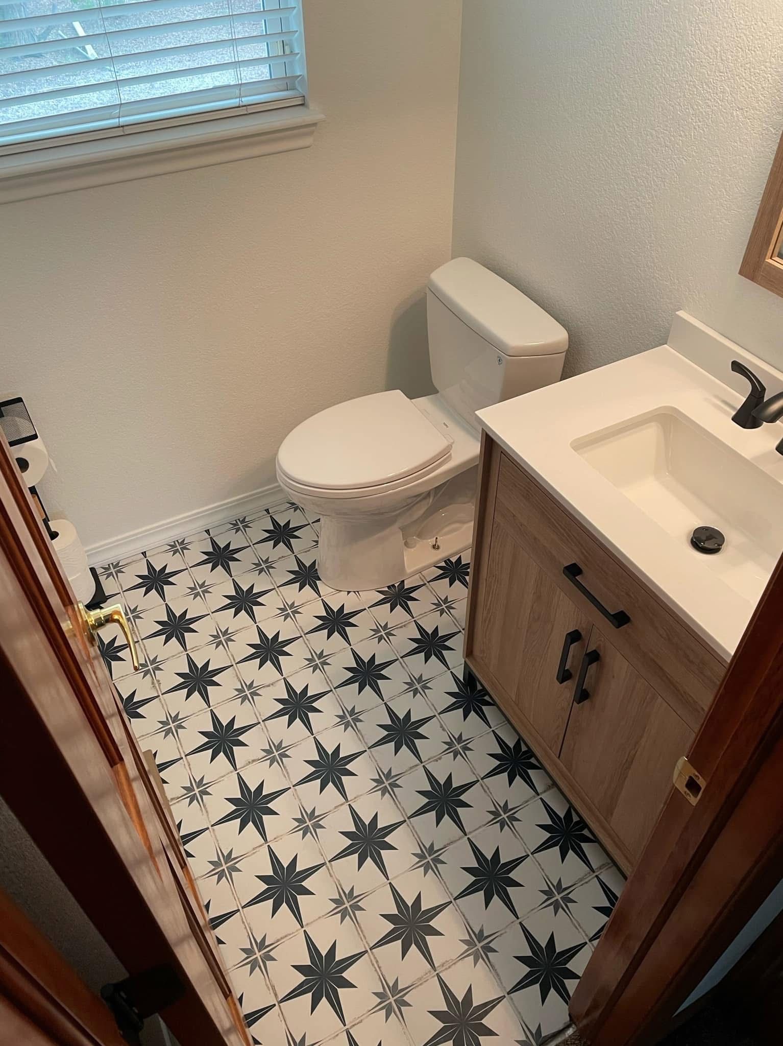Renovated compact bathroom features a white toilet, wood vanity, integrated sink, matte black faucet 