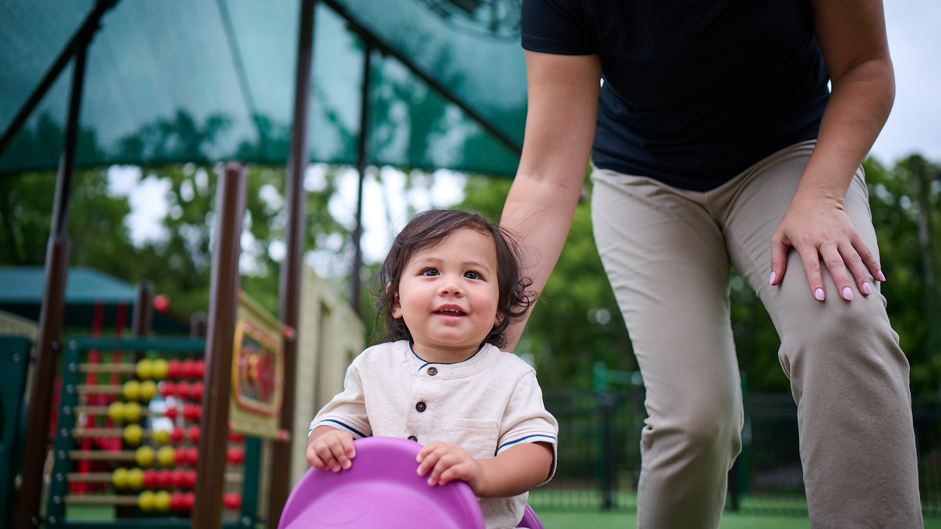 Primrose Schools teacher supervising toddler on purple slide at outdoor early childhood playground
